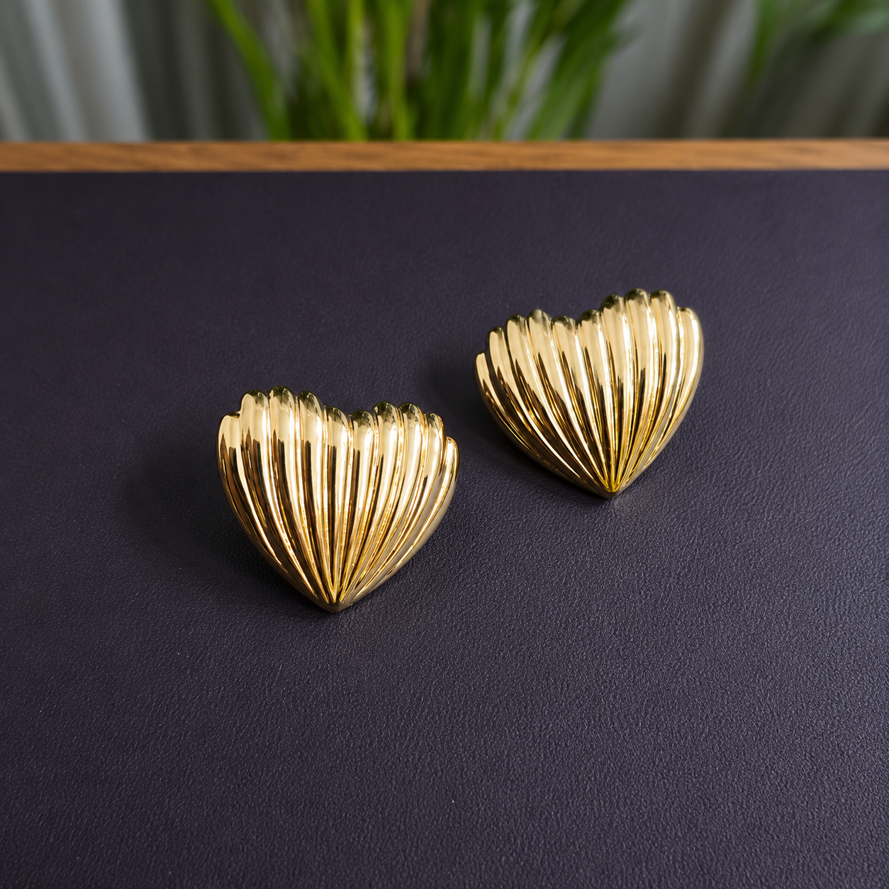 Flaire Studio ribbed gold heart stud earrings on dark surface